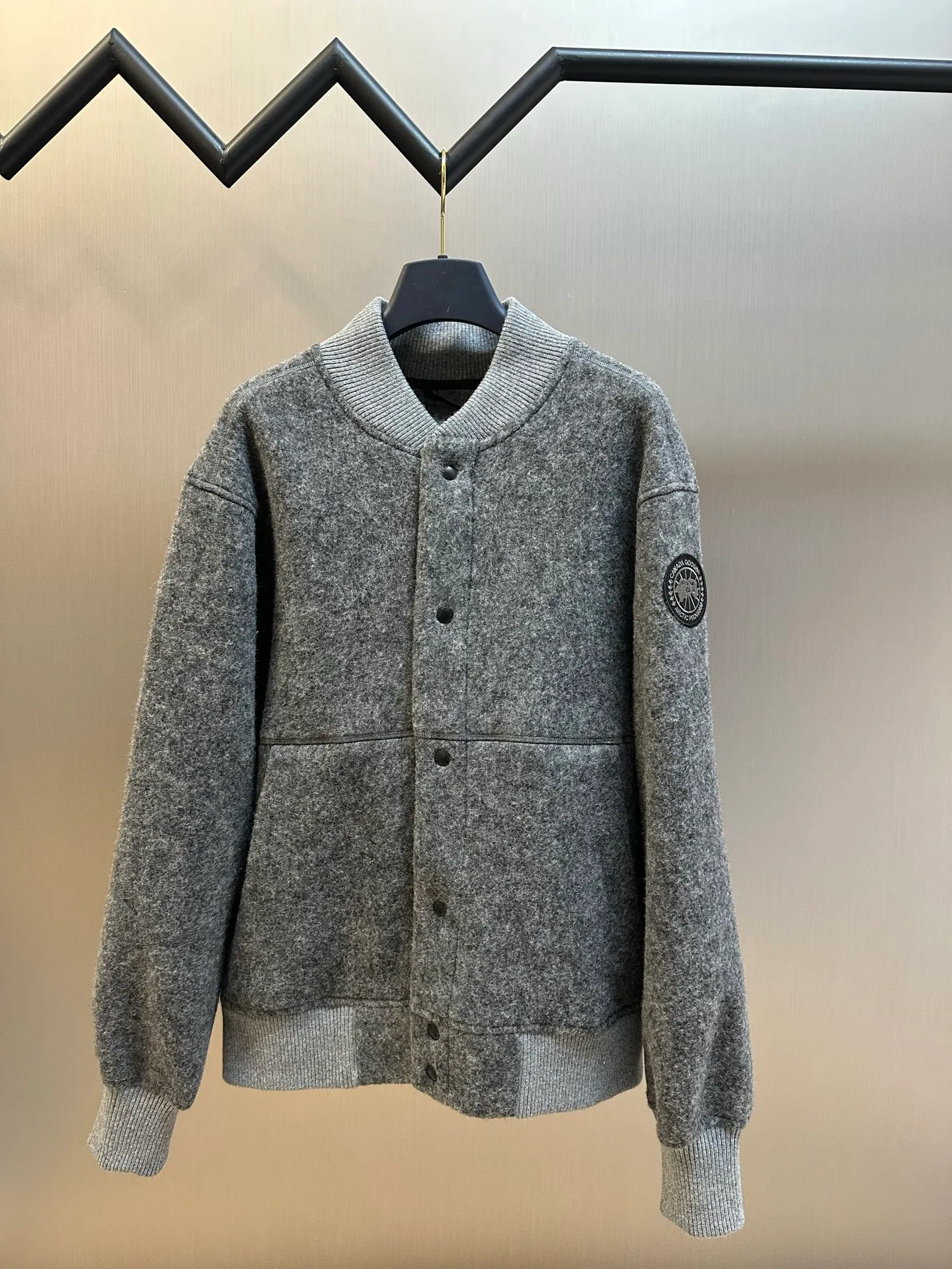 P770 Canada Goose Fleece Badge Button Jacket The main fabric of this jacket is light gray wool blend fabric to improve the fabric's wear resistance, wrinkle resistance and warmth. Wool provides good warmth and a natural feel, while blended fibers enhance the fabric's practicality and durability.  The cutting process needs to ensure that the texture and color of the fabric are evenly distributed, especially with this light gray tone, to avoid chromatic aberrations. The stretchability of wool-blend fabrics needs to be taken into consideration when cutting pieces to ensure dimensional stability of the finished garment.  Use a sewing needle and thread suitable for wool-blend fabrics to avoid damage to the fabric during sewing. The sewing stitches are even and firm to prevent thread stripping.  The temperature needs to be controlled during ironing to avoid high temperature damage to the fabric while keeping the fabric smooth and crisp. The front and back body parts, sleeves and other main parts are stitched with flat seams to ensure a smooth silhouette. Align the fabric texture at the splices to keep the look neat.  The white circular armband on the left arm is an important part of the brand identity and is finely sewn to ensure it is strong and flat.  size：s m l xl